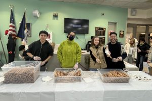 High School age students and adults stand behind a table serving churros.