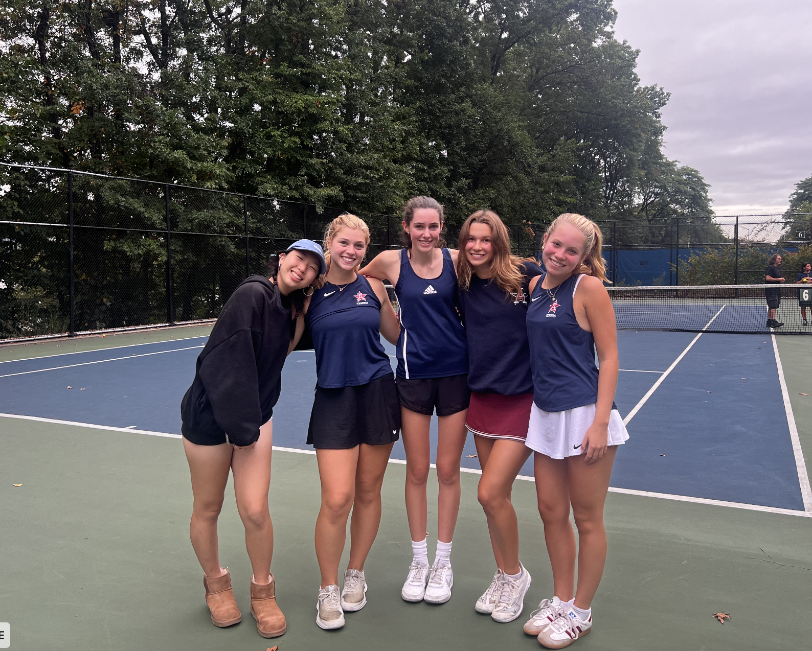 Five team members of the Girls Tennis team stand with arms over one another shoulders