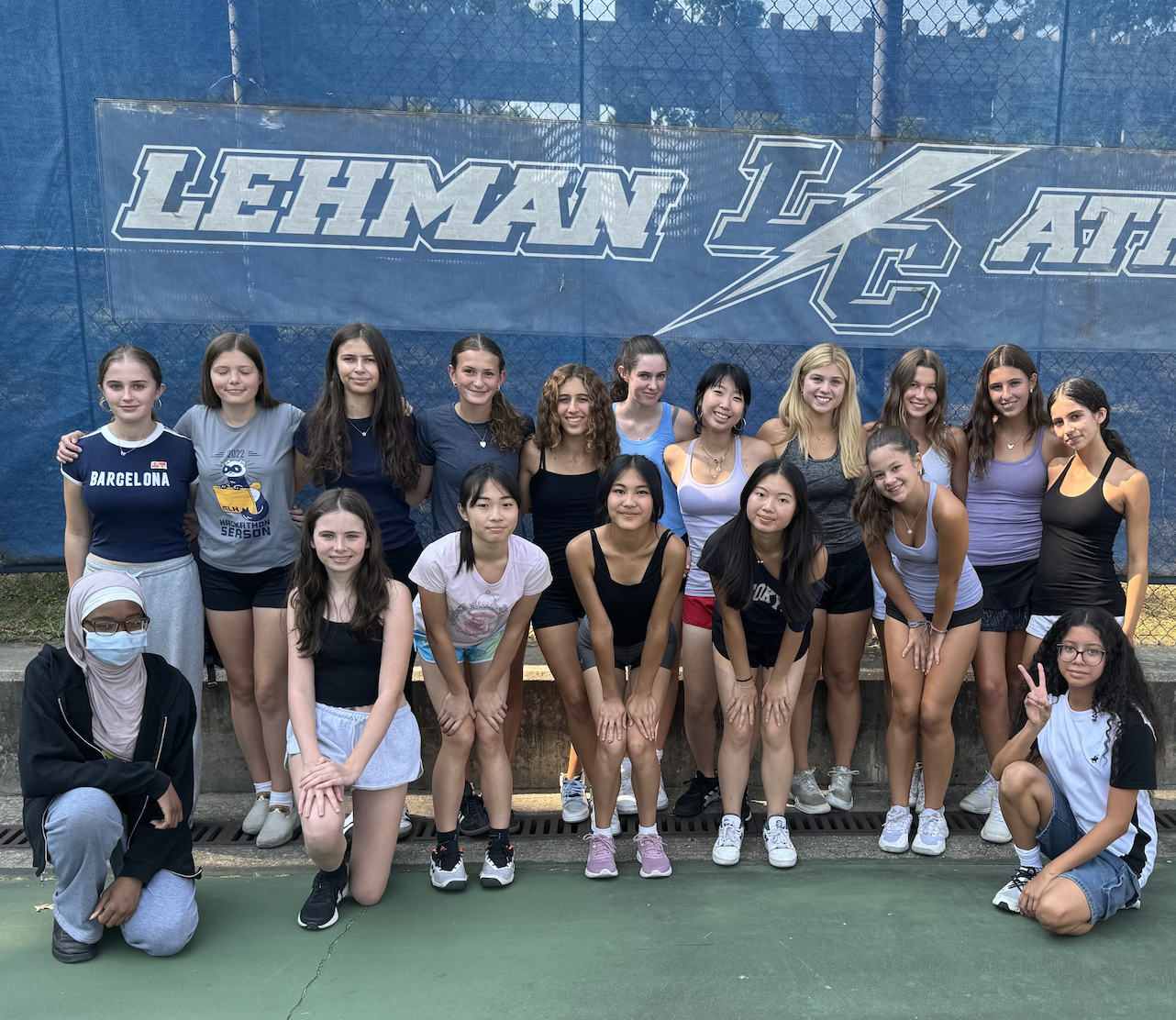 Members of the Girls Tennis team stand in front of a fence.