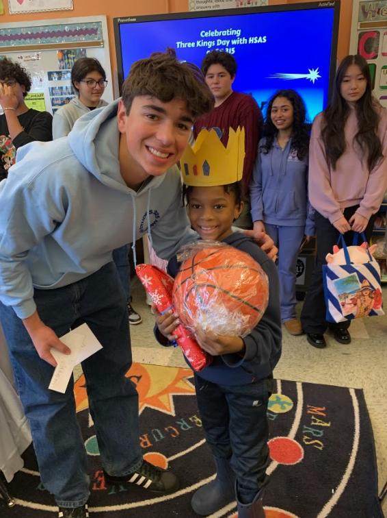 A teen student bends to pose with a elementary student holding a basketball.