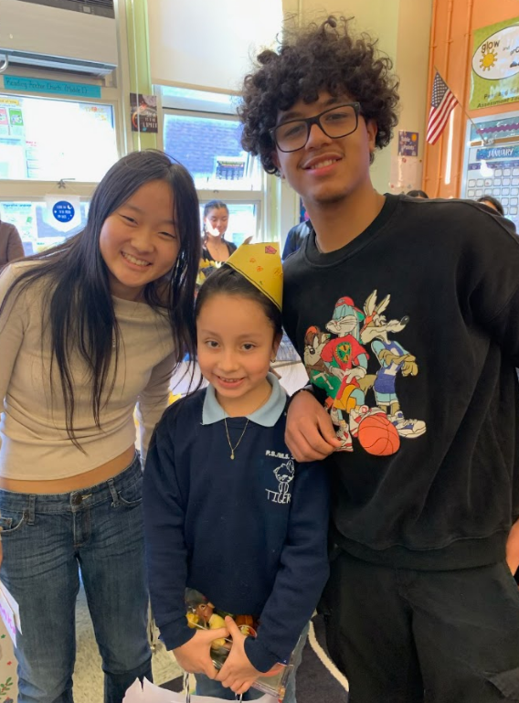 Two teenage students stand on either side of an elementary age student.