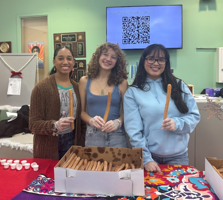 Three young women stand side by side holding churros