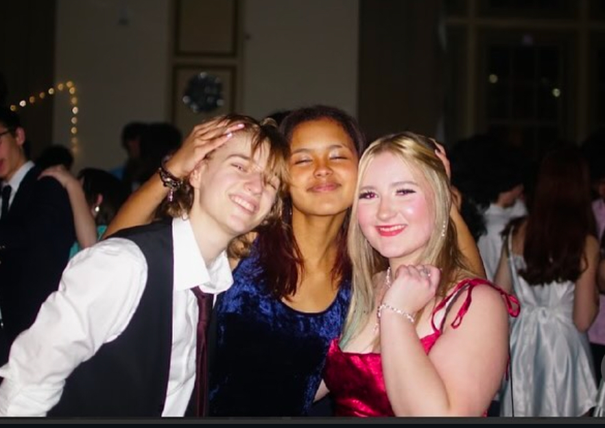 Three students estand side by side embracing one another.