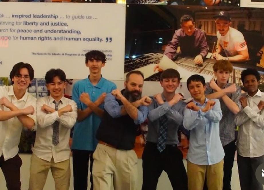 Students stand on either side of a teacher posing for the camera with their arms as an X.