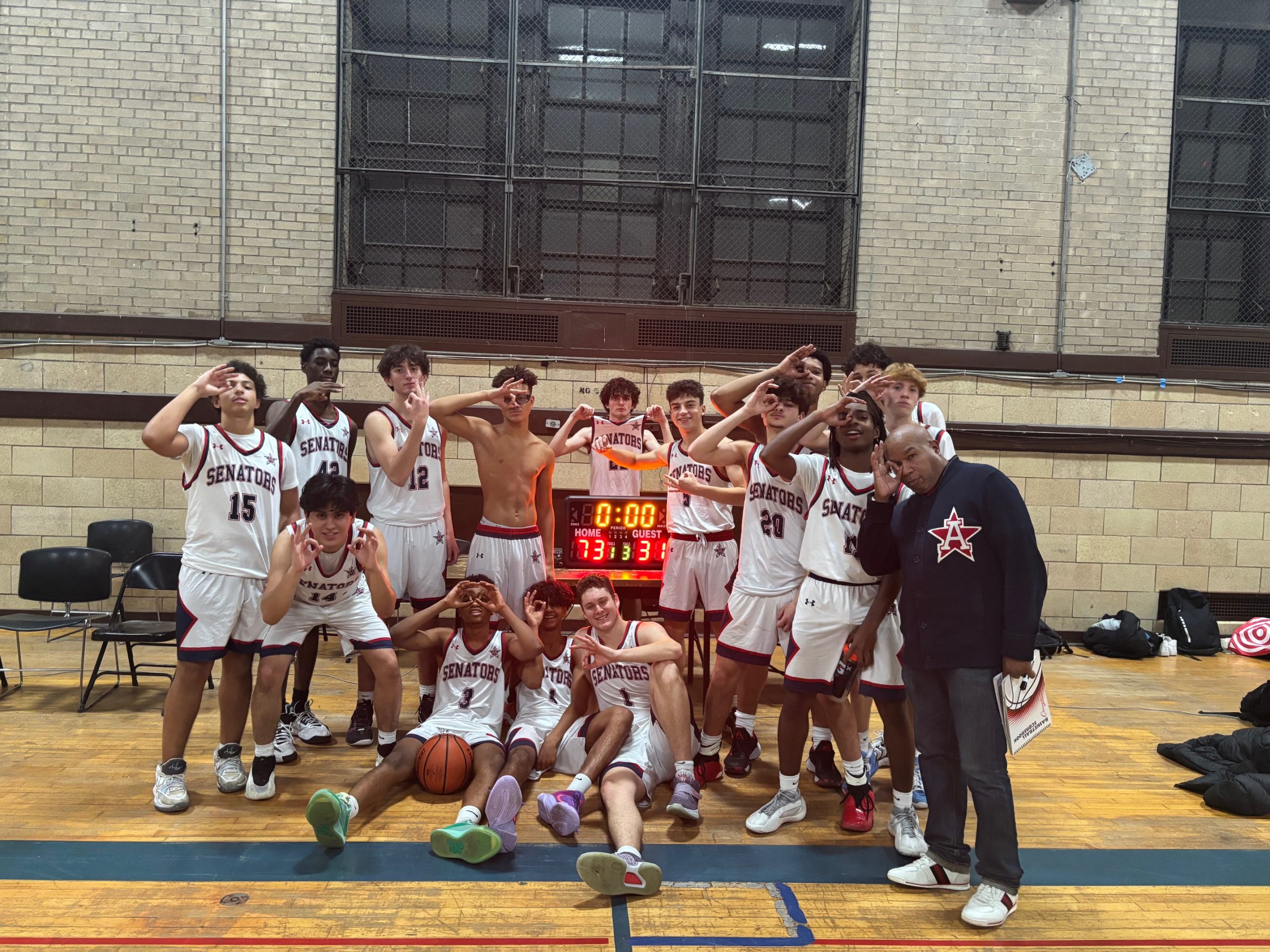 Members of the boy's basketball team pose in two rows holding their hands over their eyes in the shape of goggles with three fingers raised.