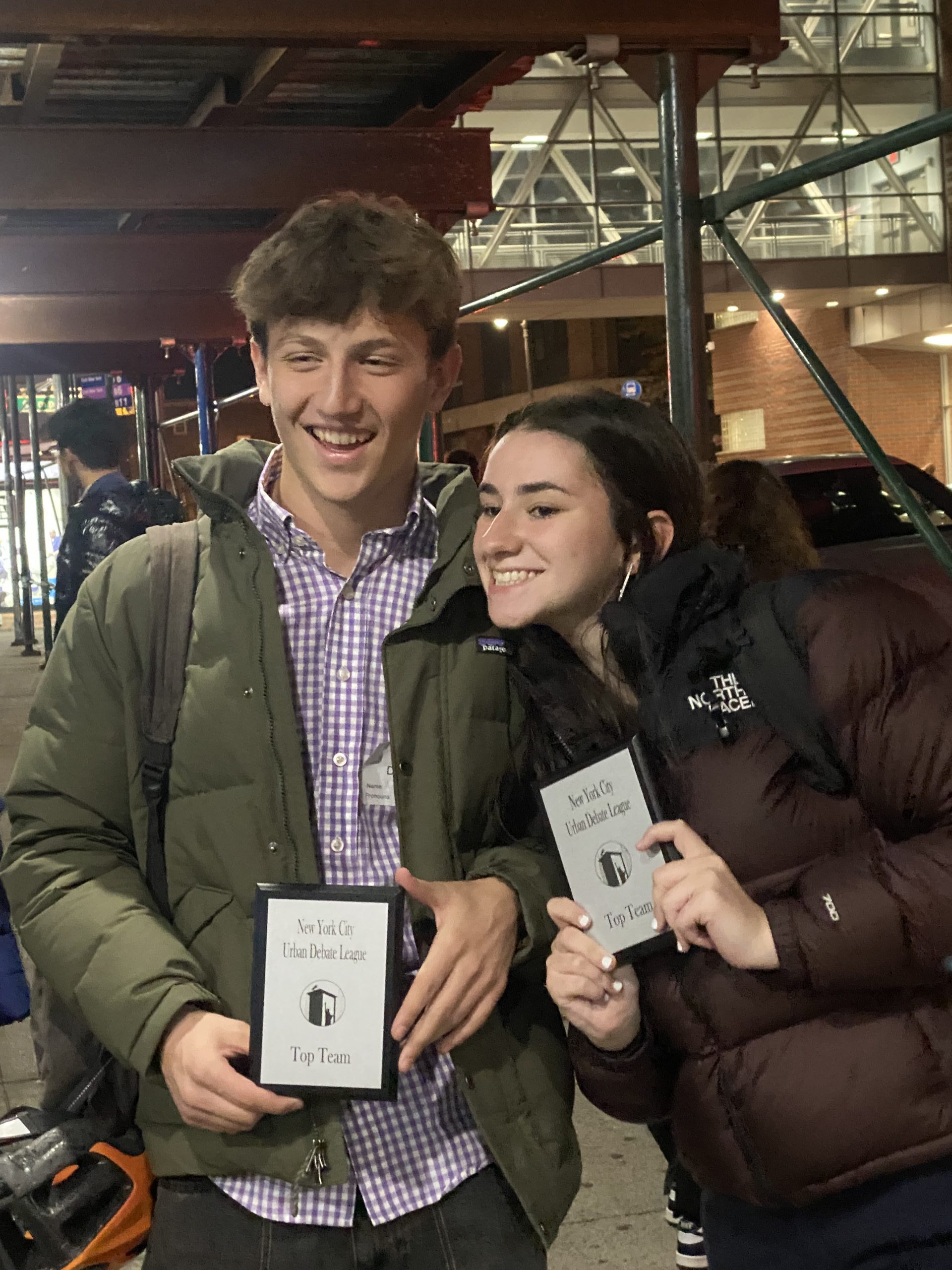 Two students stand while holding awards and smiling.