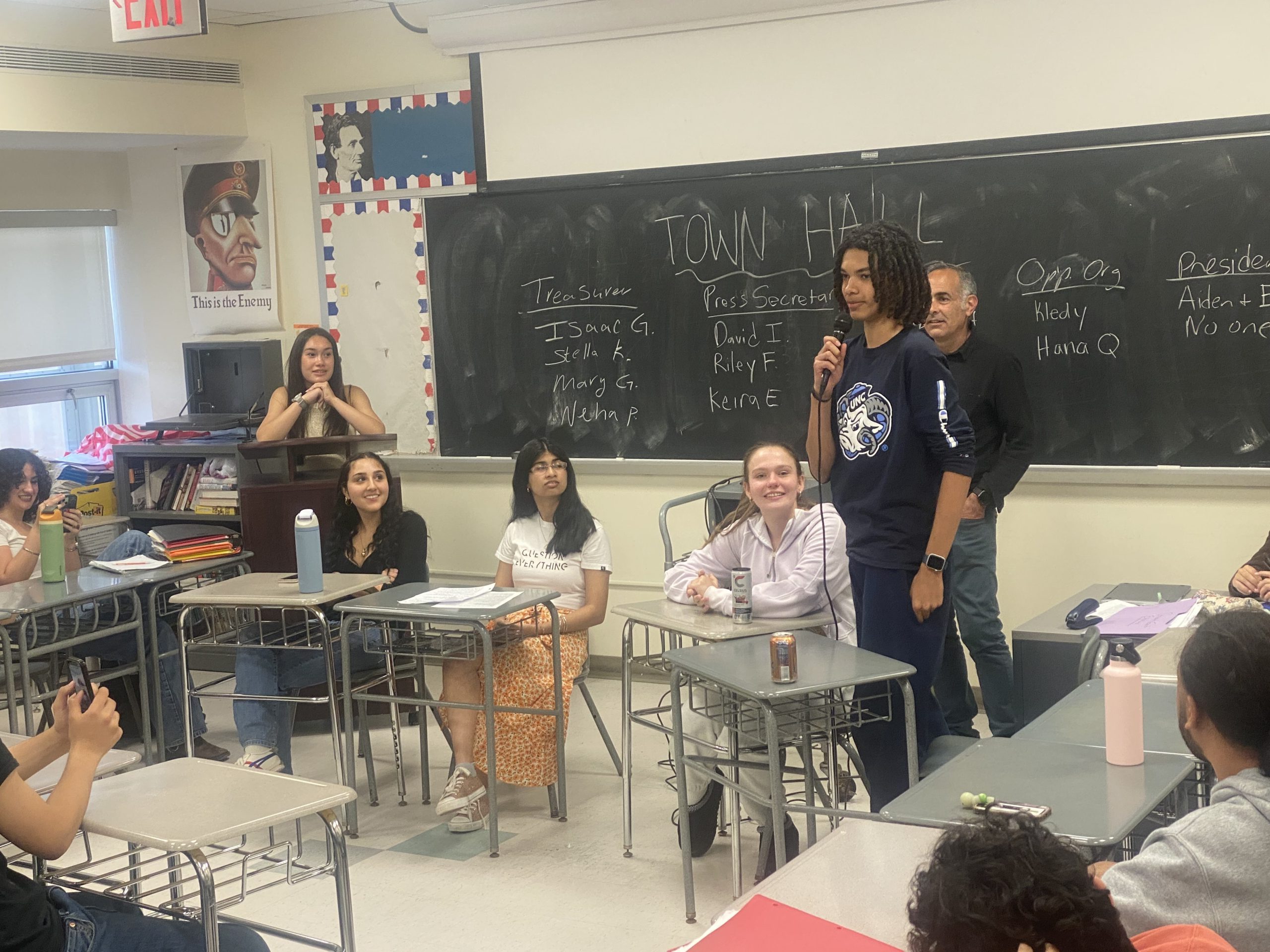 Students seated at the front of a classroom listen and turn towards to the other as they answer questions.