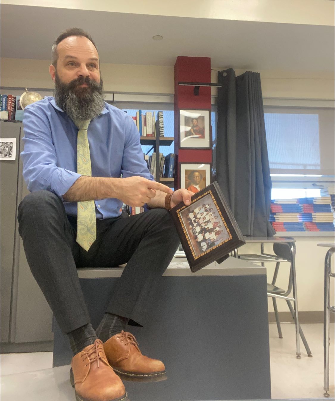 Man sits on desk holding a picture frame.