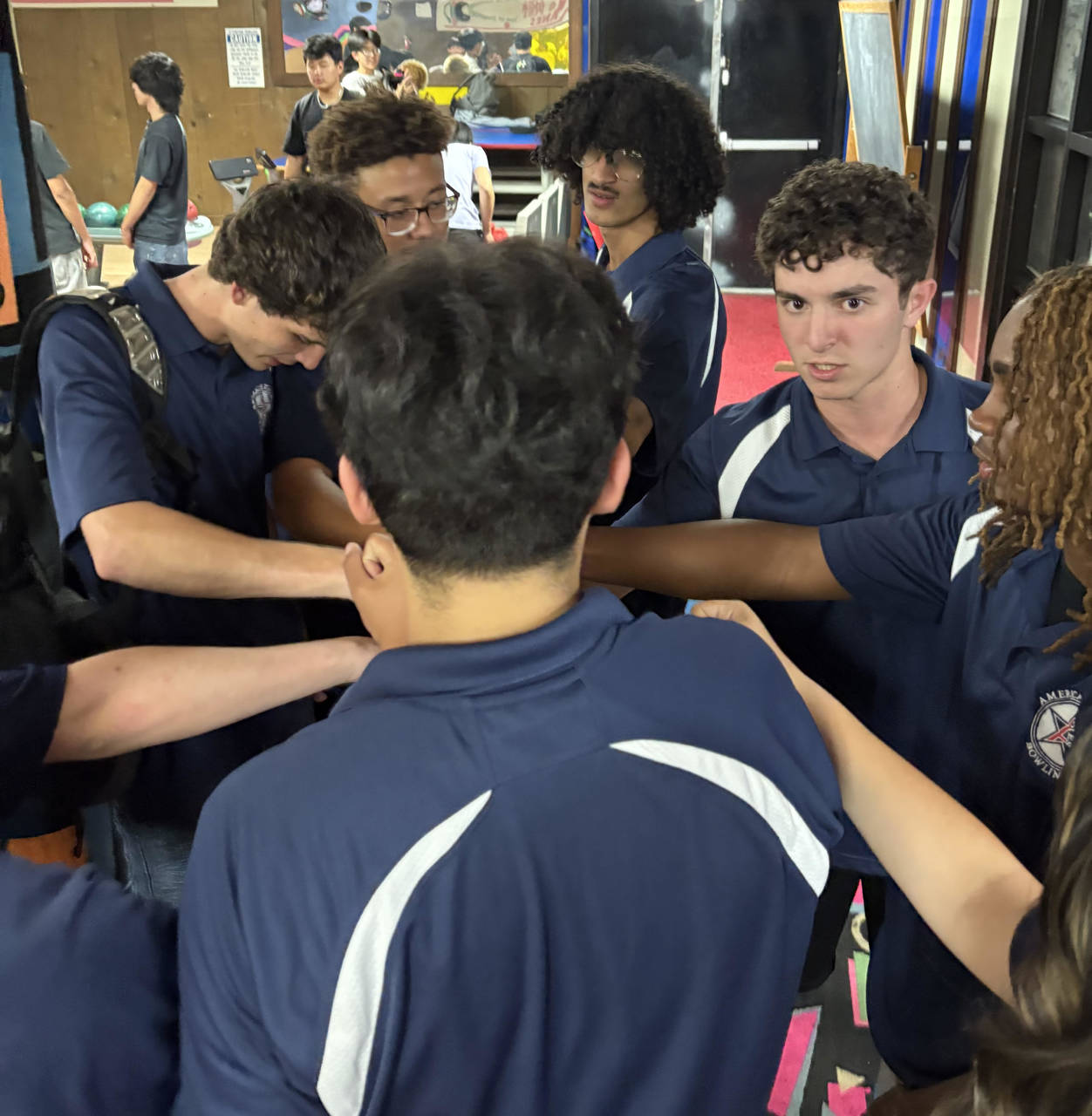 Bowling team members stand in a circle with their arms extended to the center.