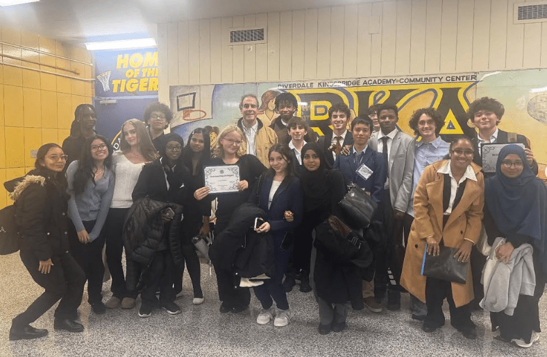 Students stand in three rows, side by side, holding awards in their hands.