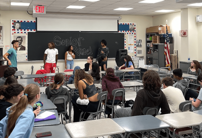 A classroom with seniors standing at the front.