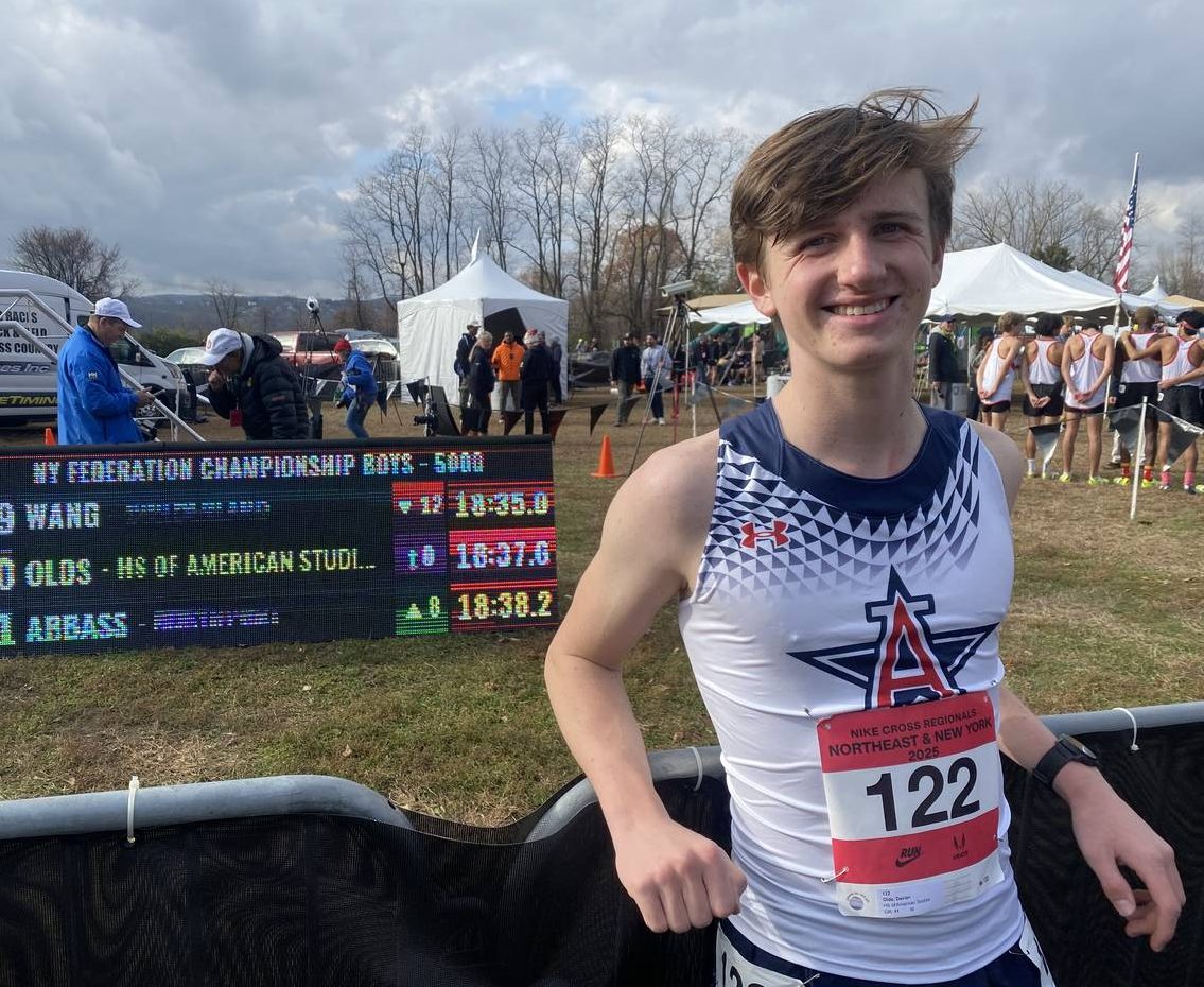Athlete stands in front of a score board with his name on it.