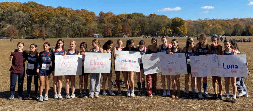 Members of the Girl's running team stand shoulder to shoulder holding signs
