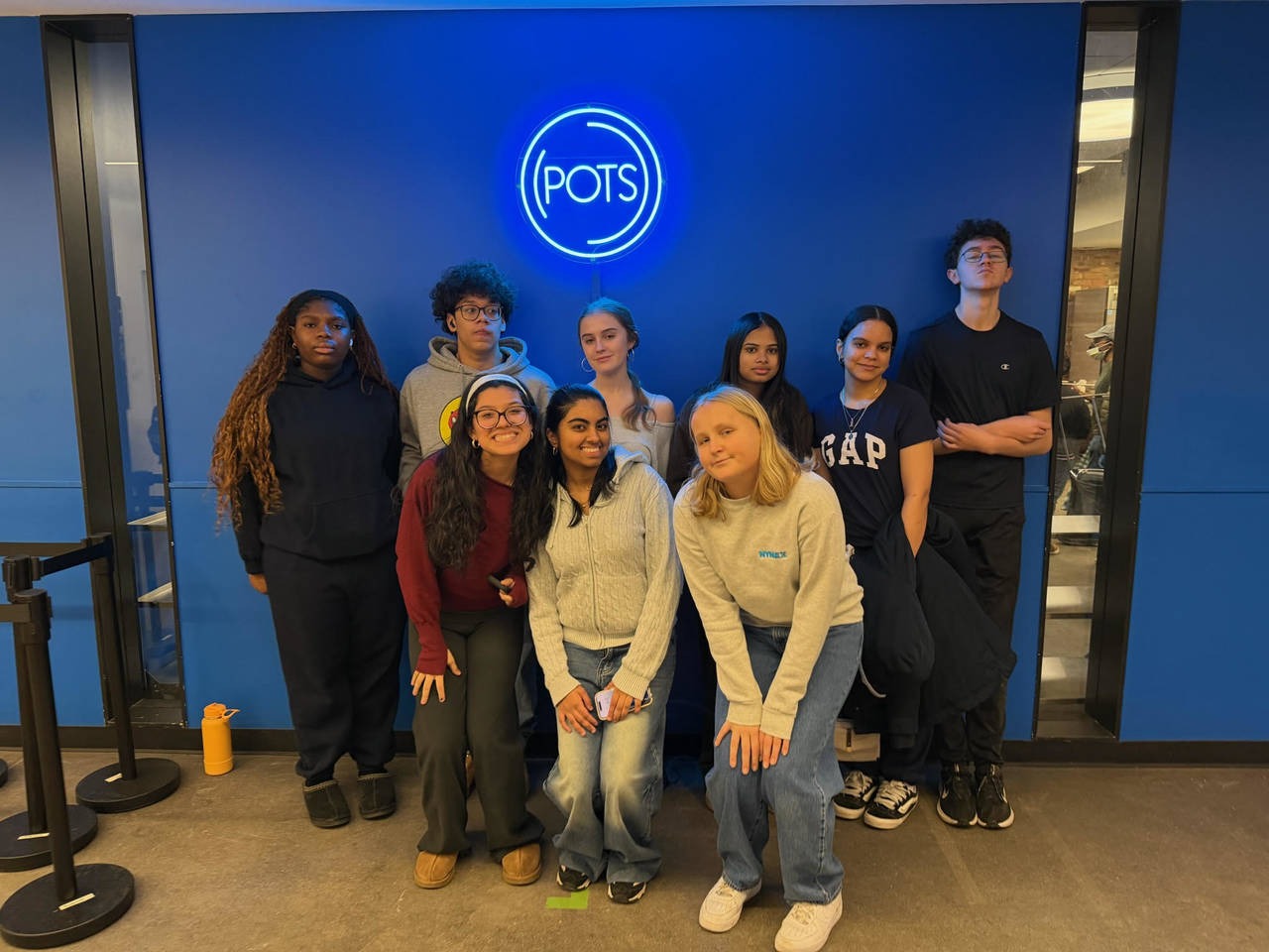 Students stand in two rows shoulder to shoulder in front of a sign that reads POTS