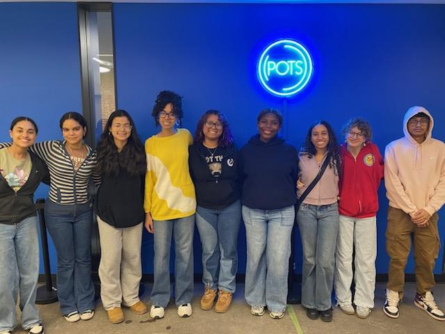 Students stand shoulder to shoulder in front of a sign that reads POTS