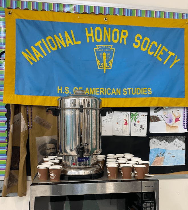 A large hot water dispenser sits on a table surrounded by dozens of cups.