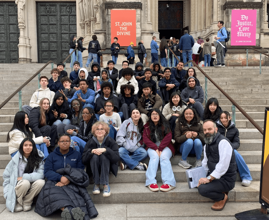 Students sit on the steps of a cathedral, sitting in 7 rows.