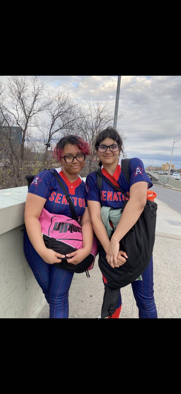 Two students pose side by side in softball uniforms