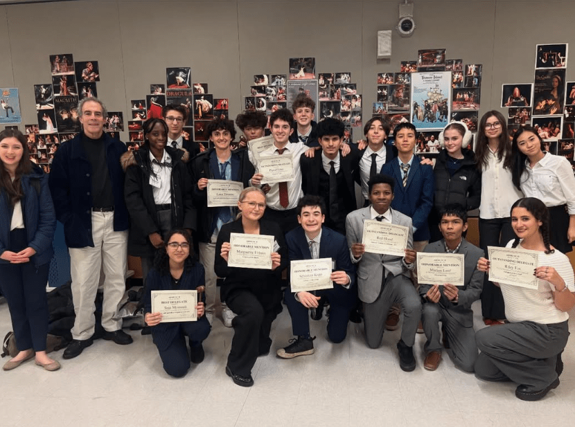 A dozen students stand behind students kneeling holding up certificates.