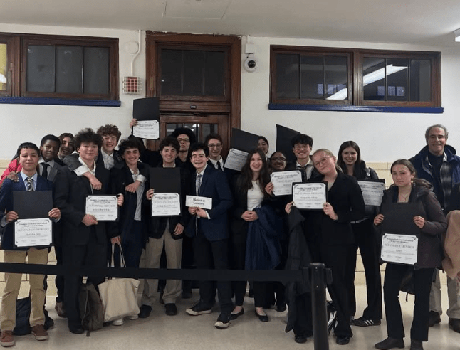 A dozen students stand in three rows holding up certificates.