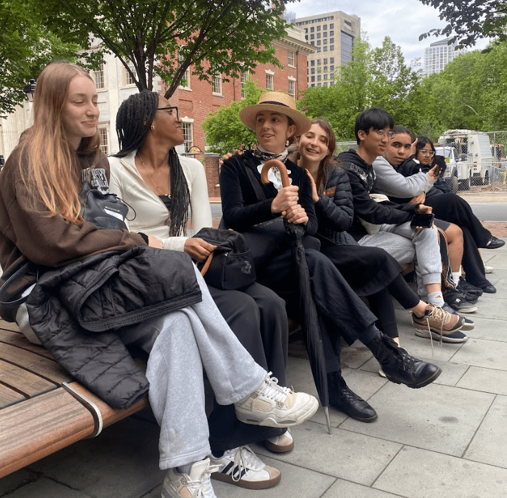 7 students sit on a bench having a discussion.