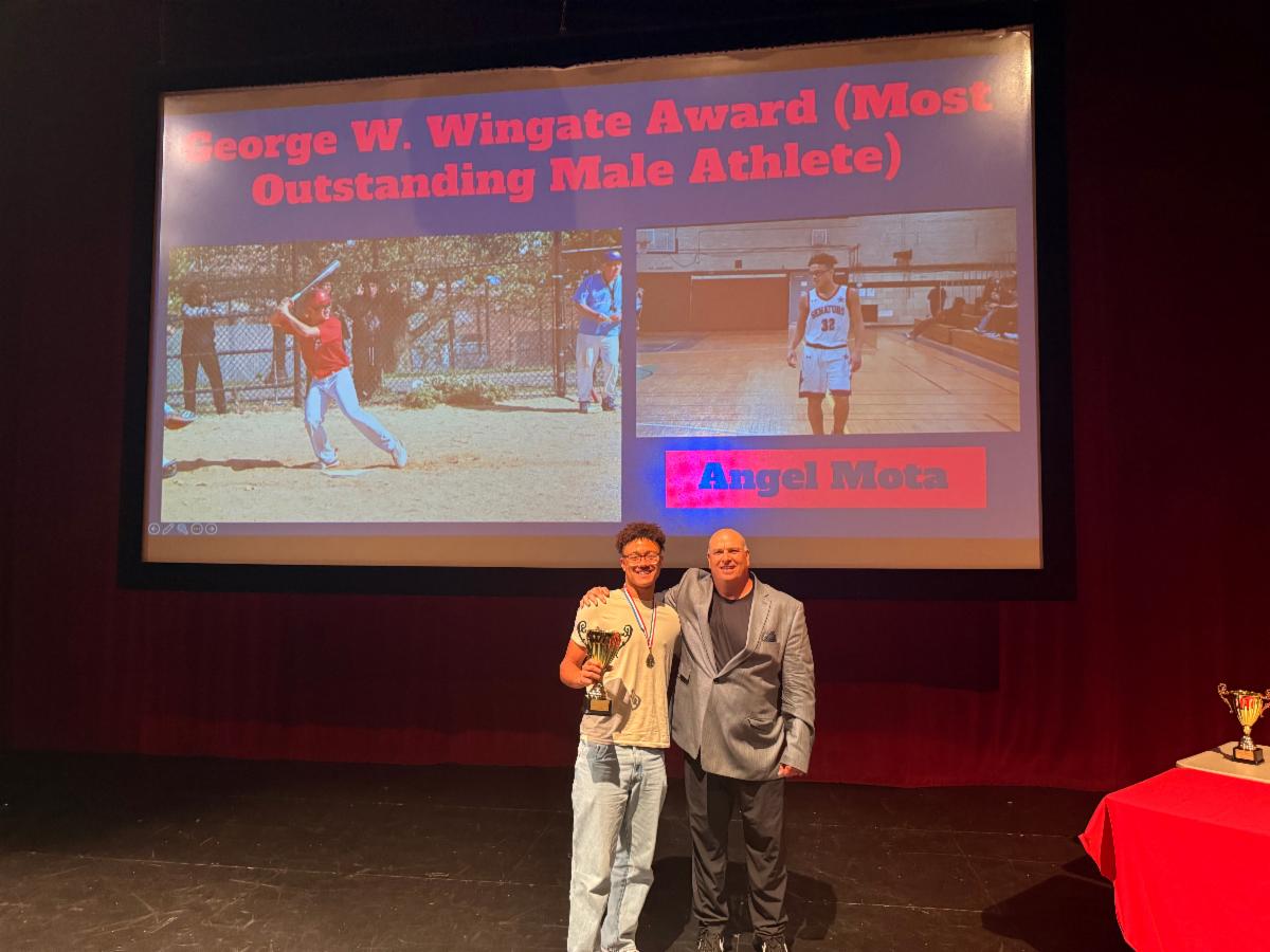Student stands with a coach holding an award on stage.