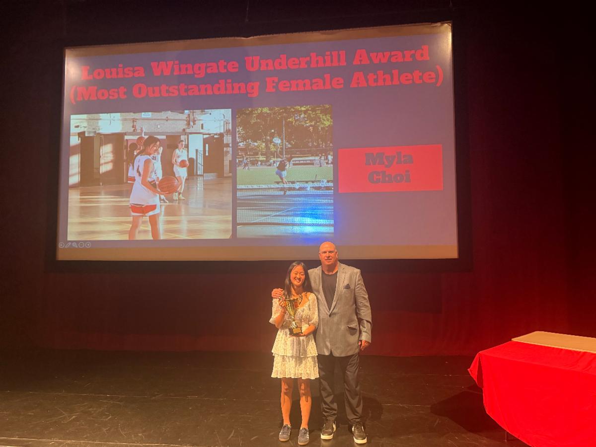Student stands with a coach holding an award on stage.