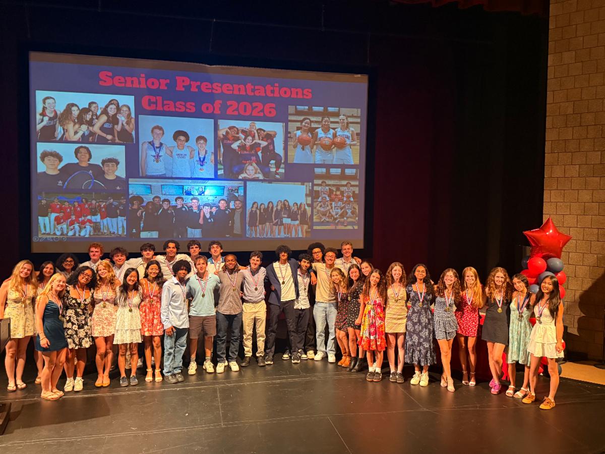 Dozens of students stand on stage in two rows.