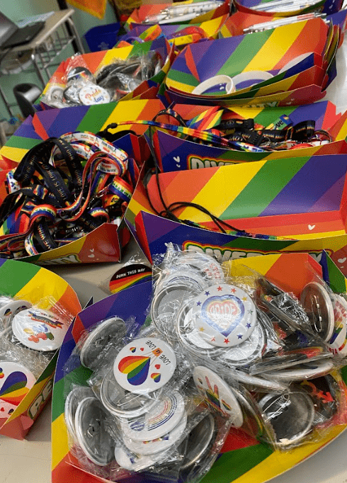 Rainbow colored pin and bracelets sit in bins on a counter.