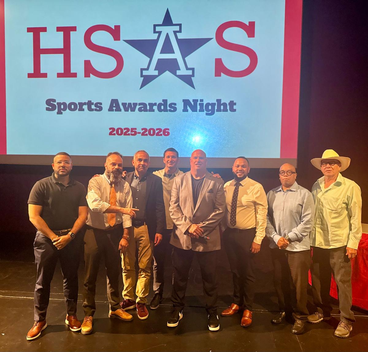 A half dozen adult coaches stand on stage.