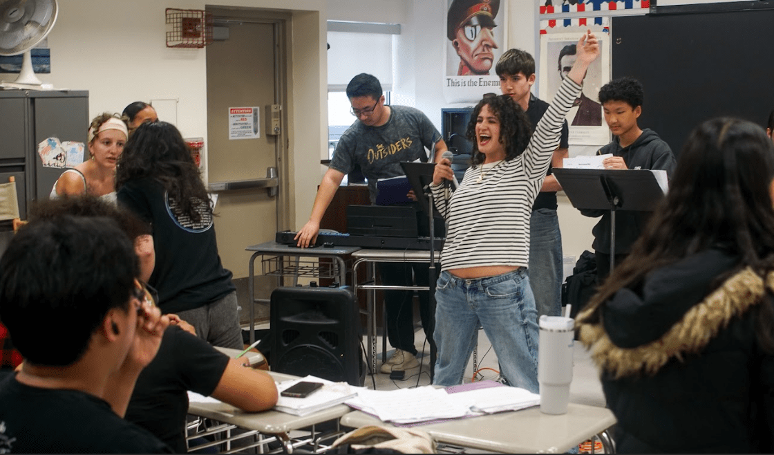 Students hold a microphone and stand in front of students.
