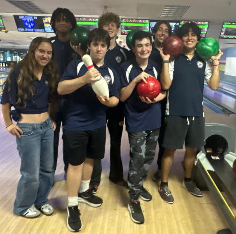 Members of the bowling team stand holding bowling balls in an alley.