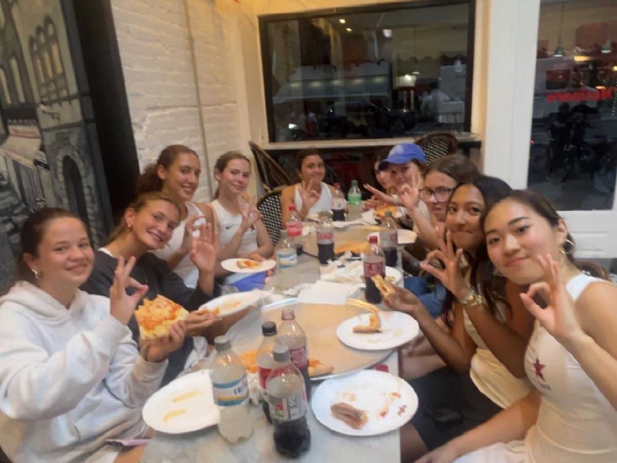 Tennis players sit at a table eating pizza.